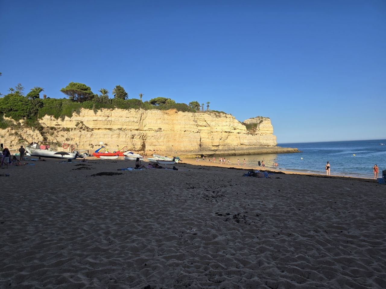 Praia de Nossa Senhora da Rocha beach with golden cliffs, small boats, dark sand, and blue sea