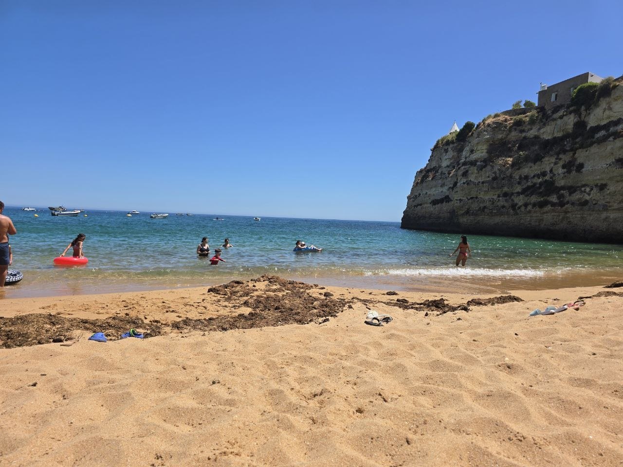 Sunny shoreline at Praia de Nossa Senhora da Rocha with limestone cliffs and swimmers