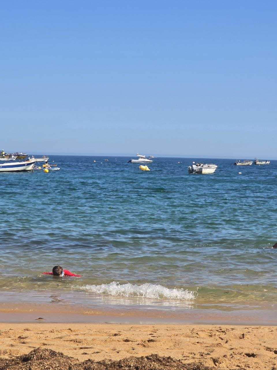 Noah swimming near the shore at Praia de Nossa Senhora da Rocha with small boats offshore