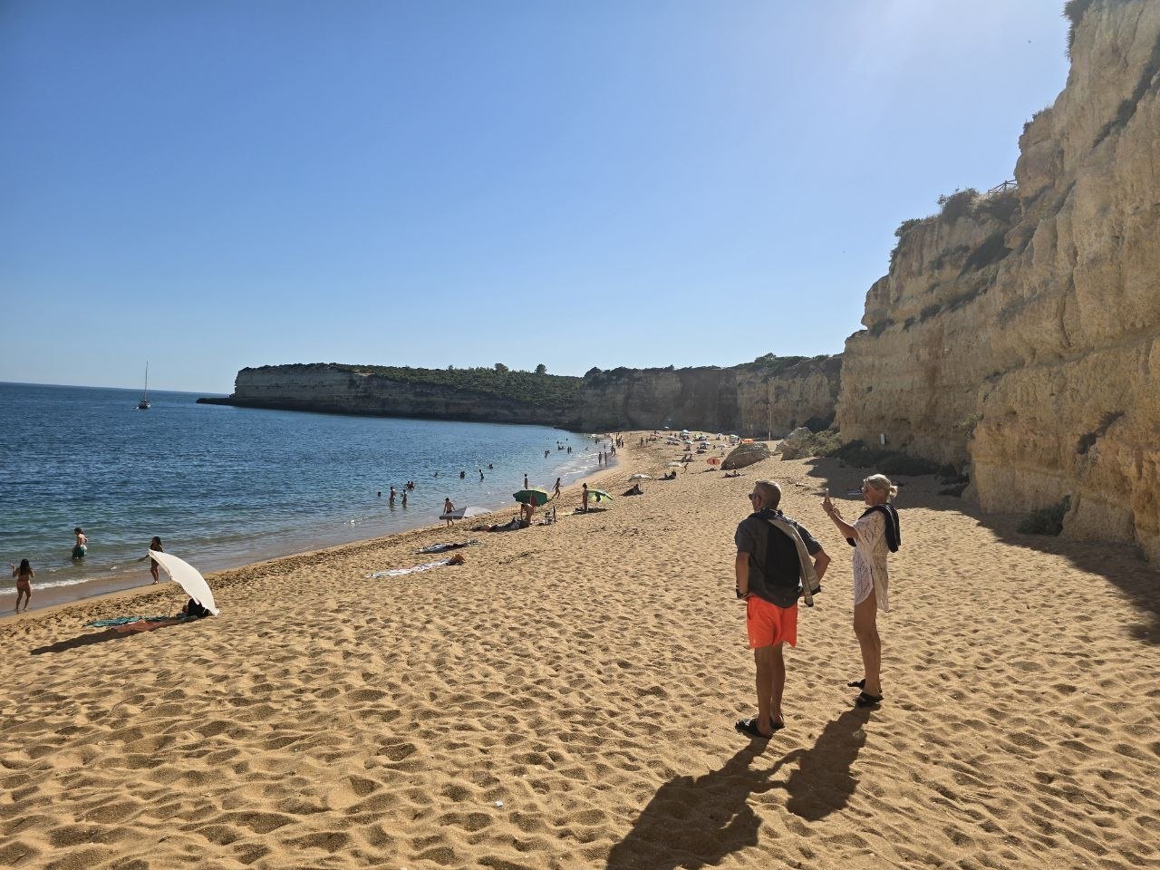 Family walking along the sandy beach beneath cliffs at Praia de Nossa Senhora da Rocha
