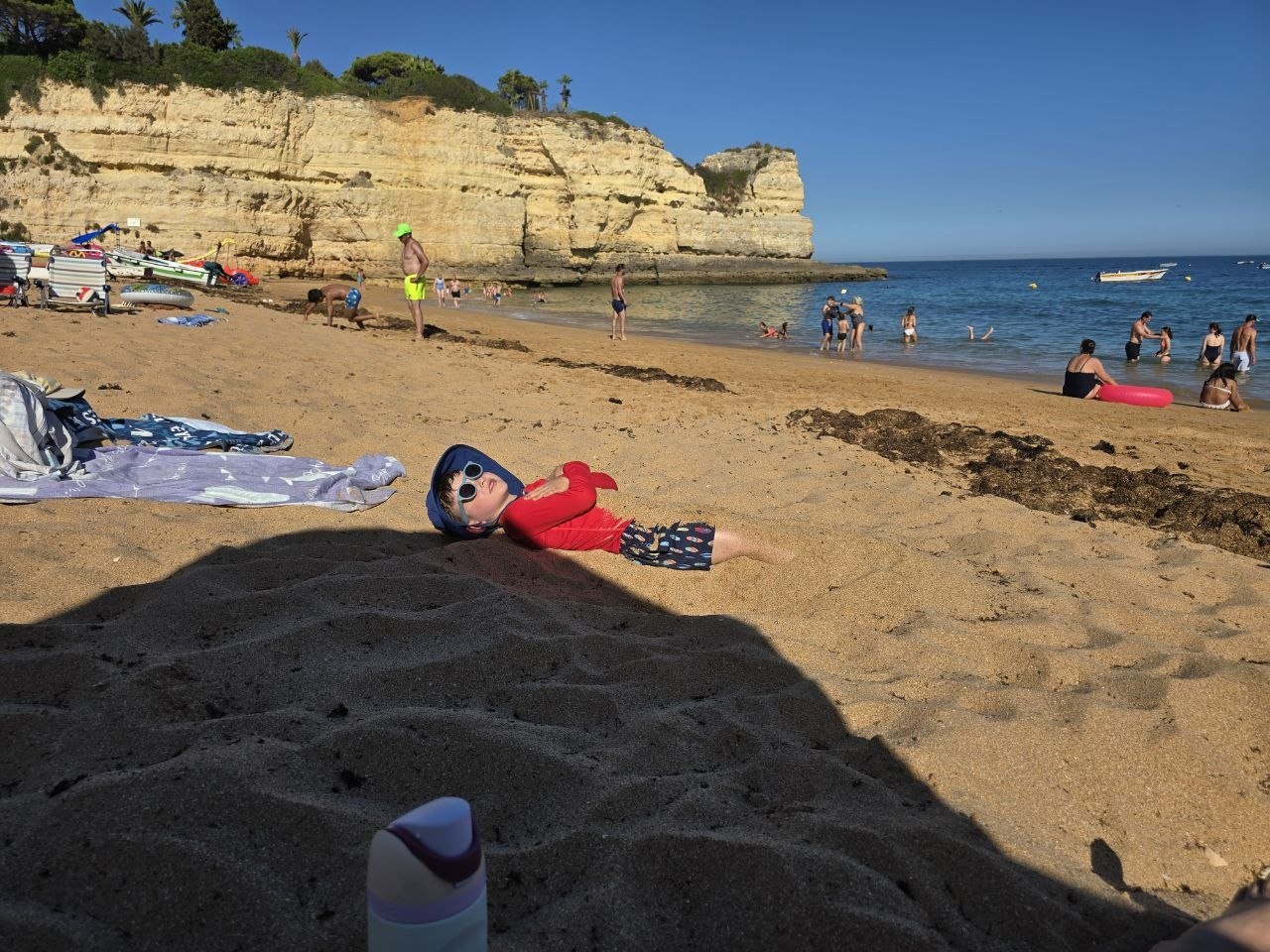Noah lying back in the sand at Praia de Nossa Senhora da Rocha with cliffs and beach behind him