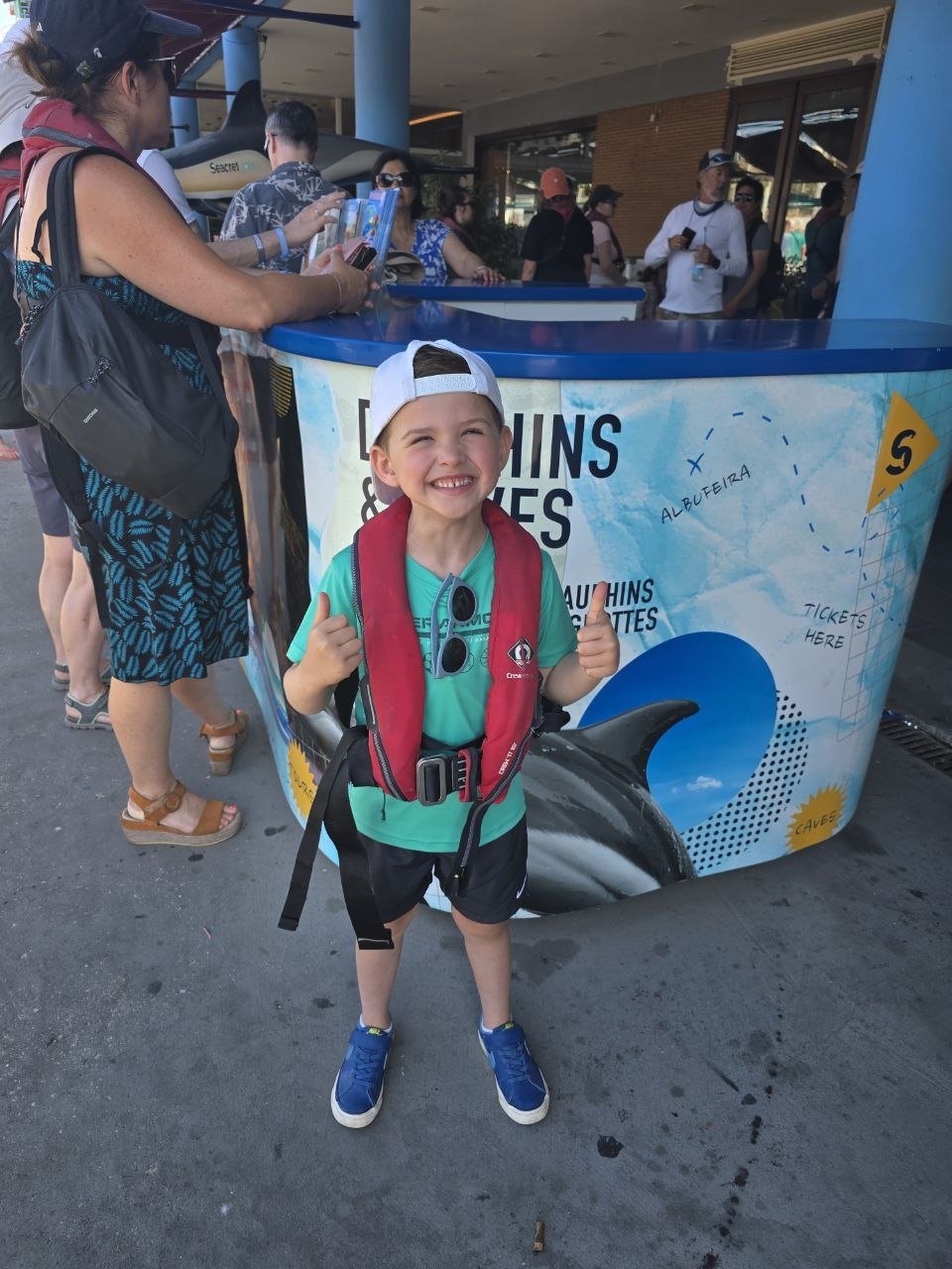 Noah smiling in a life jacket at the dolphin and caves tour check-in stand in Albufeira