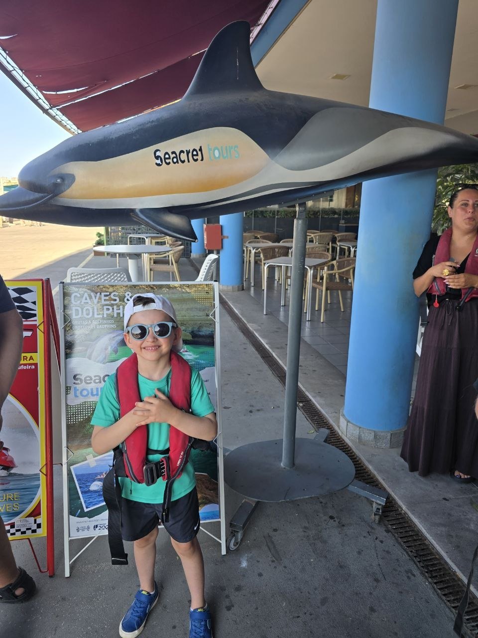Noah standing under a large Seacret Tours dolphin display before the boat tour