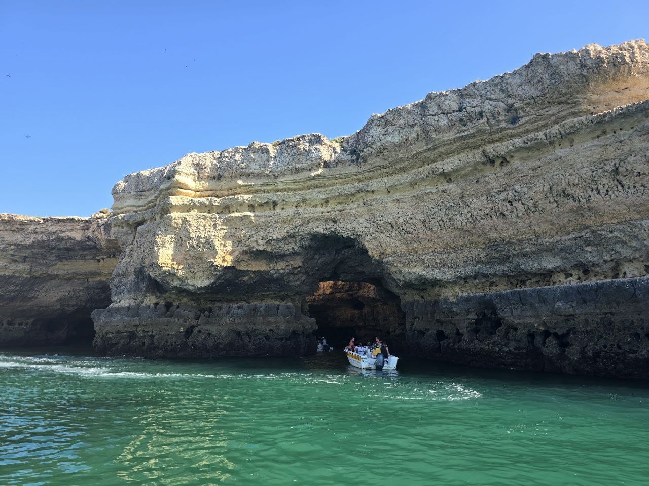 A small boat near a sea cave in golden Algarve cliffs over turquoise water
