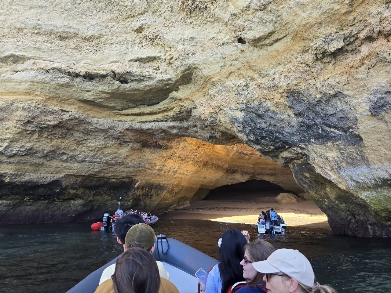 Tour boats entering a wide sea cave with a sandy beach inside