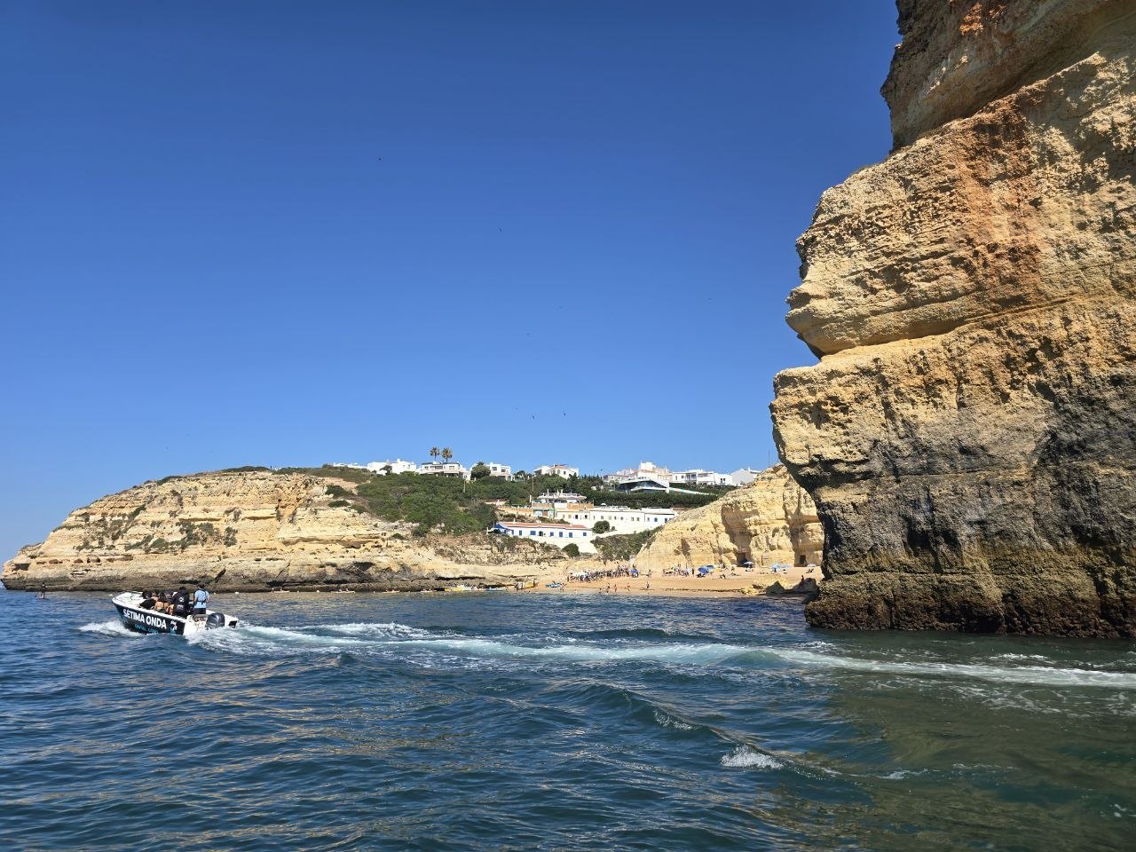 A small motorboat passing golden cliffs and a beach along the Algarve coast