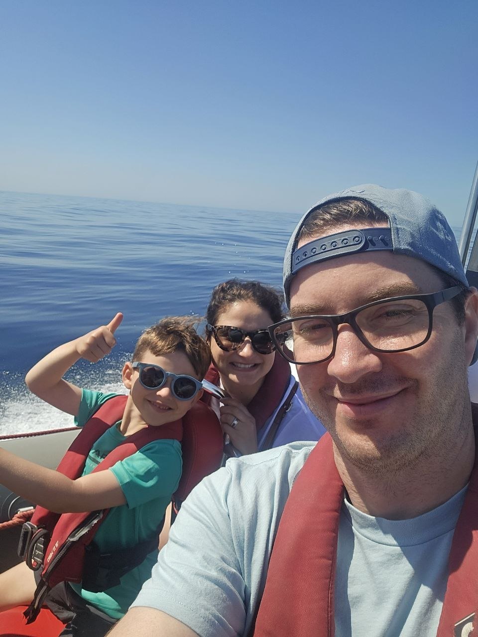 Family selfie on a zodiac boat wearing life jackets over calm open water