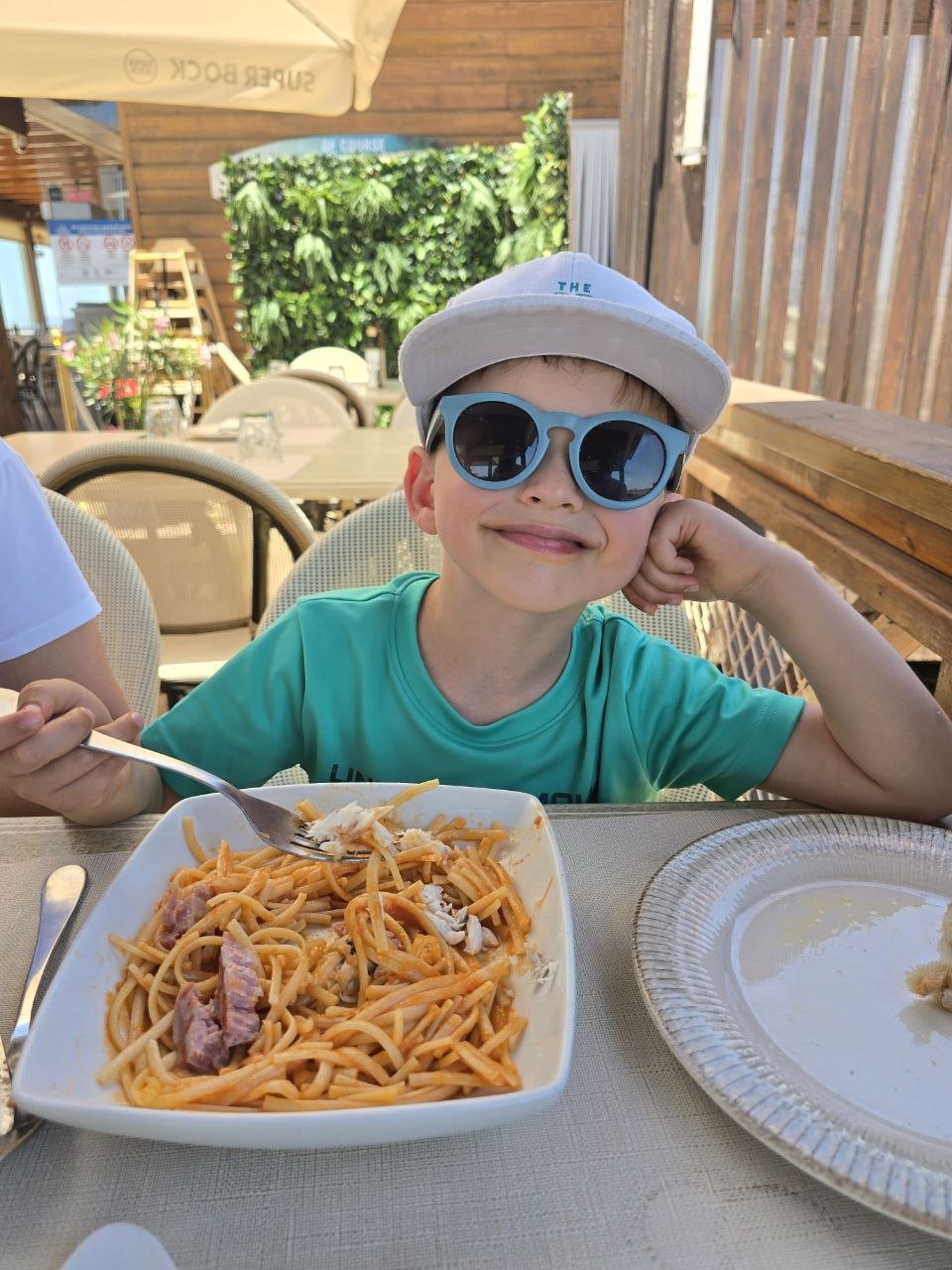 Noah smiling in sunglasses with a bowl of spaghetti at the beach restaurant