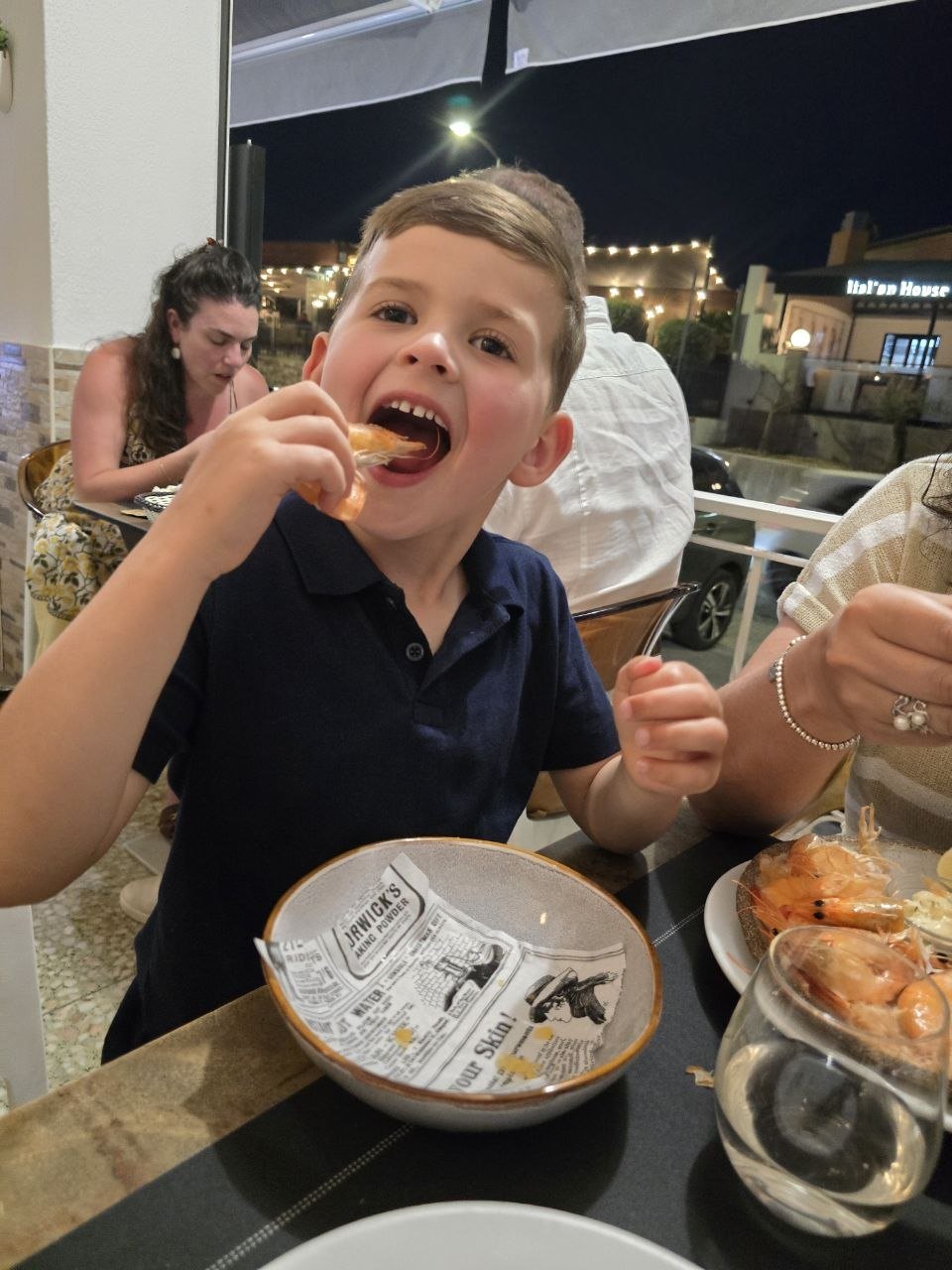 Noah smiling and eating shrimp at an outdoor restaurant table at night