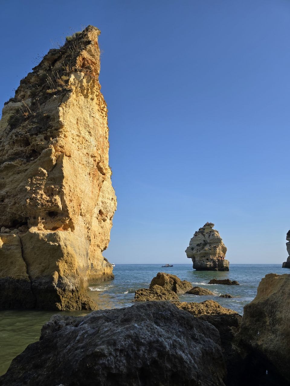Tall golden sea stack and rocks at Praia da Marinha against a clear blue sky