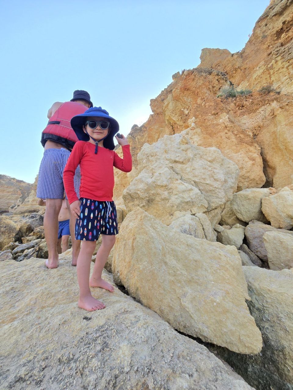 Noah standing on pale beach rocks at Praia da Marinha wearing his sun hat and sunglasses