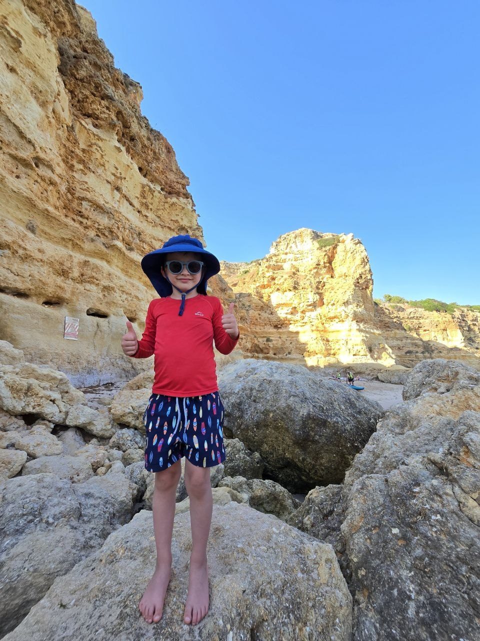 Noah standing on rocks at Praia da Marinha with cliffs and sea behind him