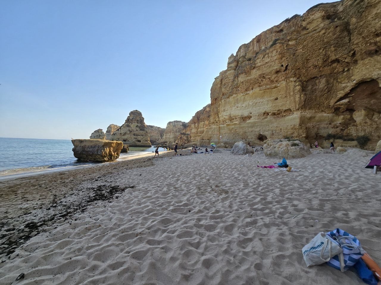 Wide sandy Praia da Marinha beach with calm water, seaweed, giant cliffs, and beach bags