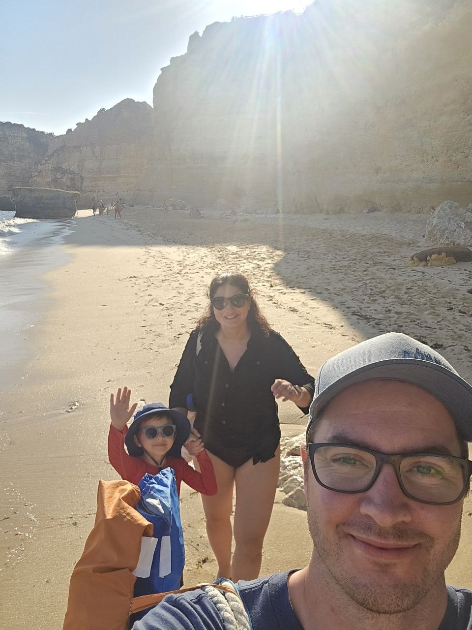 Family departure selfie on Praia da Marinha beach with bright sun, cliffs, and wet sand behind them