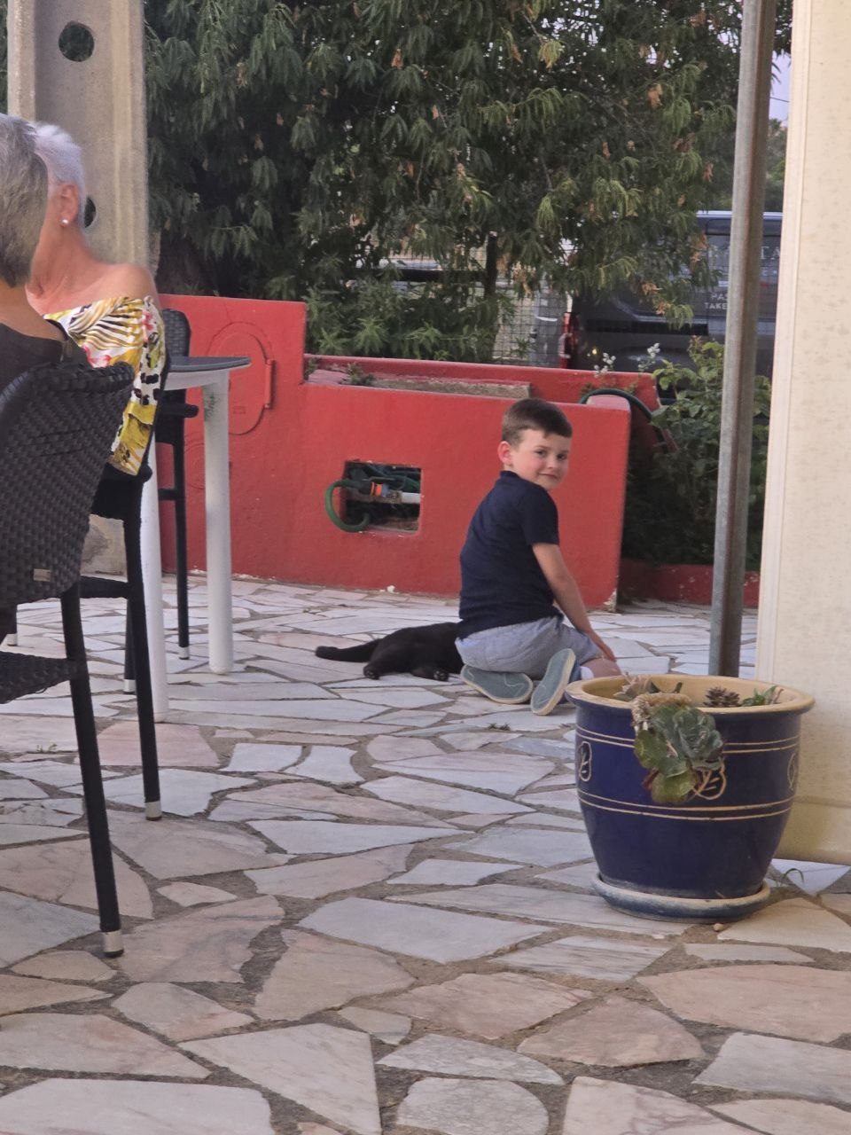 Noah sitting on the La Vera patio beside a black local cat