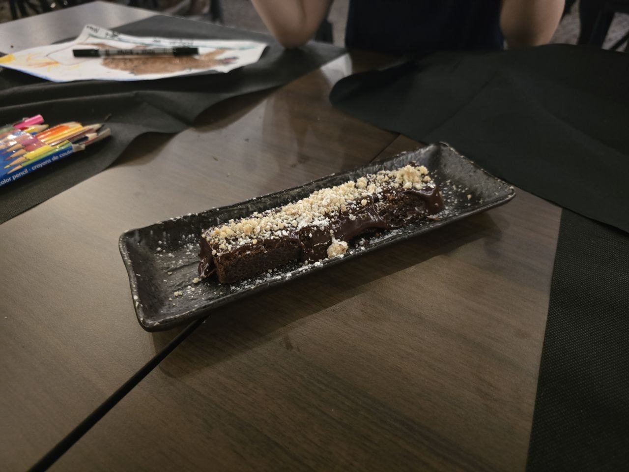 Chocolate cake with hazelnut crumble served on a black rectangular plate
