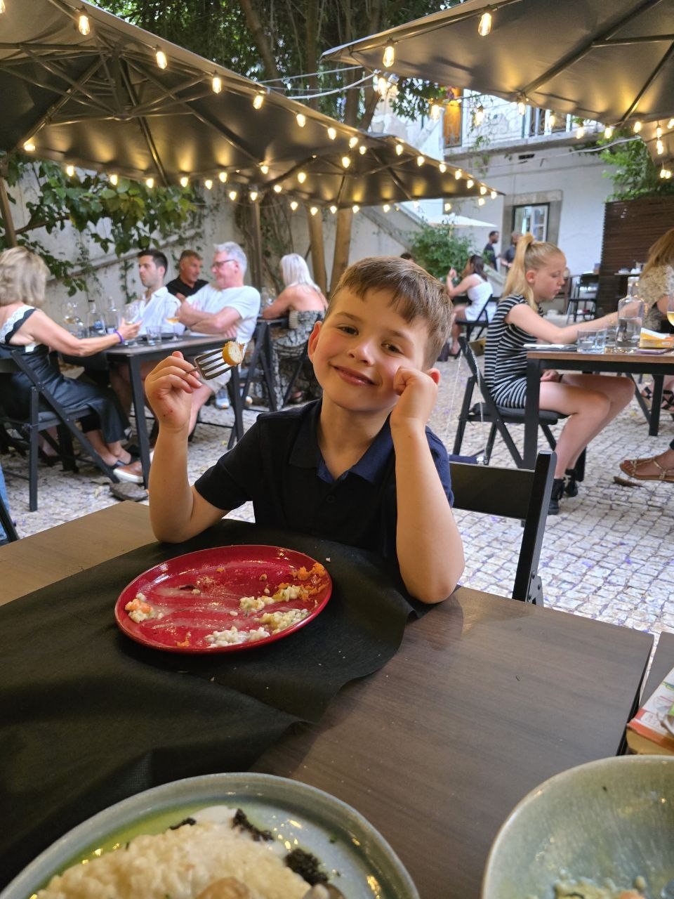Noah smiling at the patio table while holding a bite of food on a fork