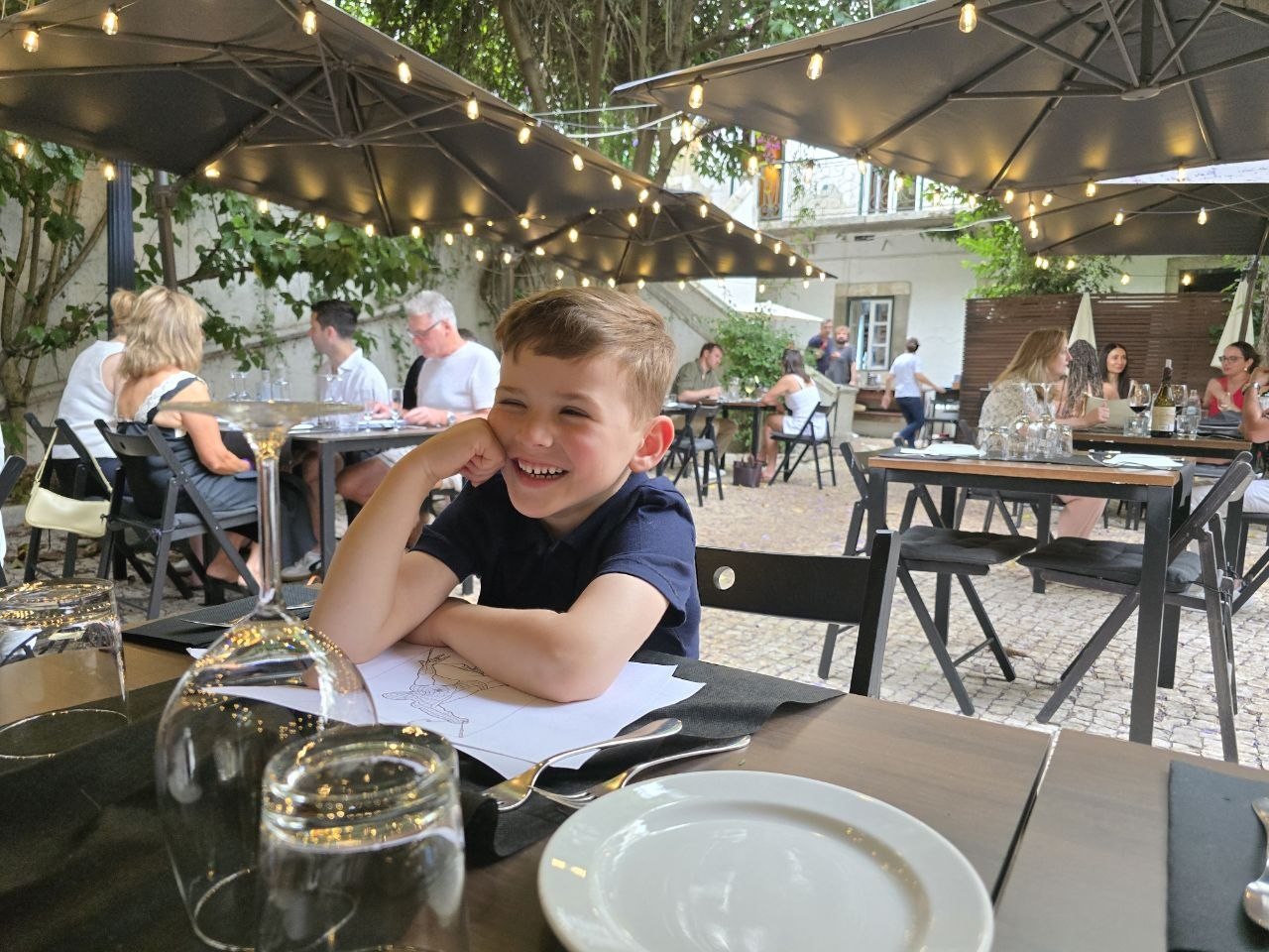 Noah smiling at the Clube de Jornalistas patio table beneath string lights