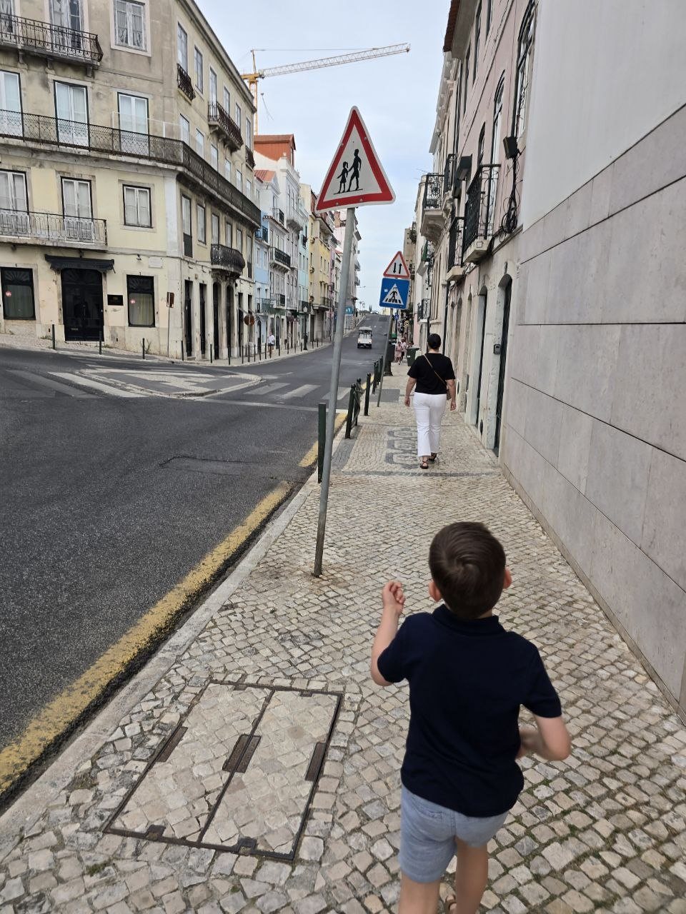 Noah walking behind Catherine on a Lisbon sidewalk from the hotel toward dinner