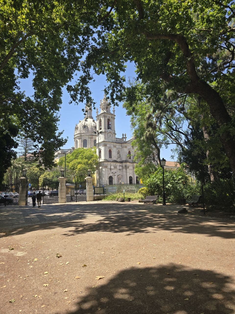White domed basilica seen through leafy trees from a shaded Lisbon garden
