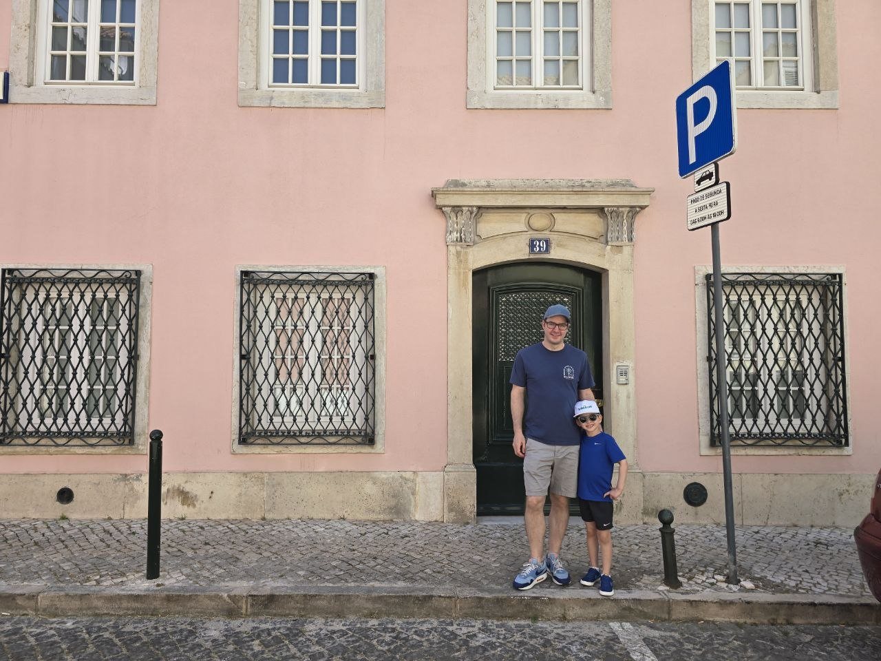 Benji and Noah standing in front of a pink Lisbon building with a black doorway in Lapa