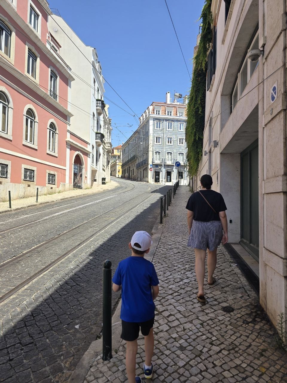 Catherine and Noah walking along a Lisbon sidewalk beside tram tracks and pastel buildings