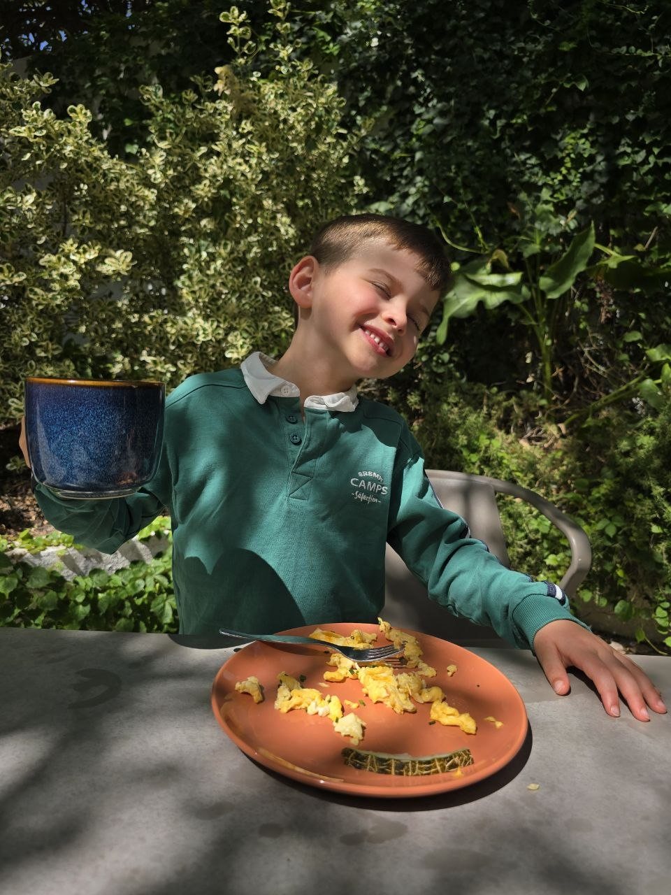 Noah smiling in the sunny Jardim da Lapa garden while holding a blue cup of morning mint tea at breakfast