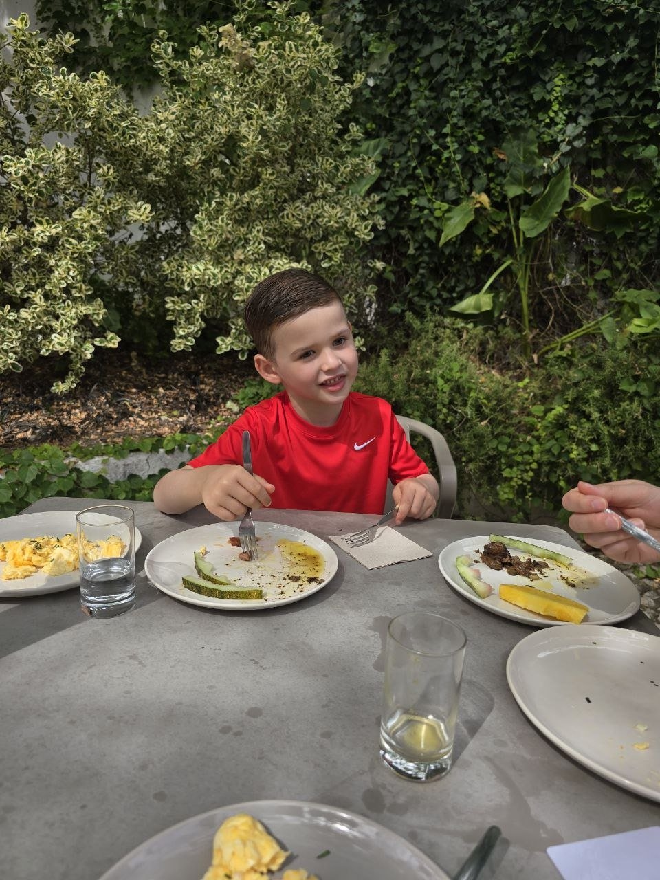 Noah smiling at an outdoor breakfast table in the Jardim da Lapa garden before the aquarium
