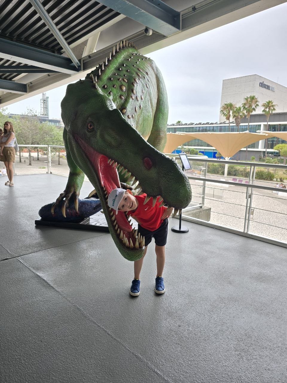 Noah posing inside the open mouth of a large green dinosaur statue near the Oceanário