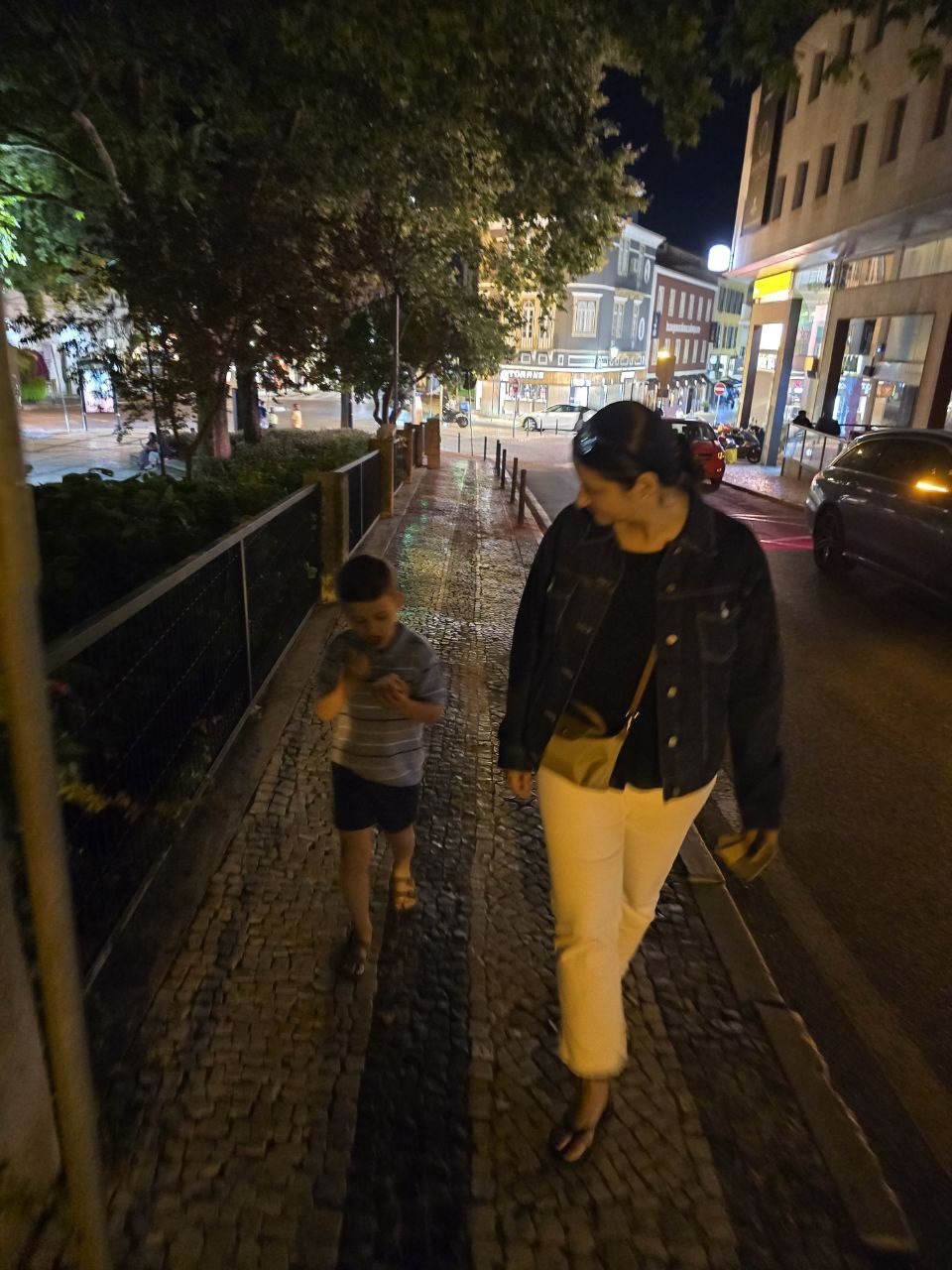 Mom and Noah walking along a lit Cascais sidewalk at night
