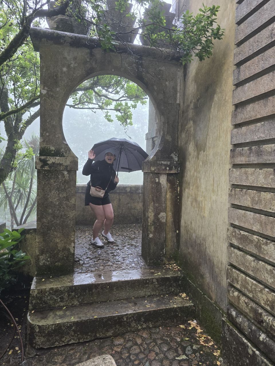 Person with umbrella walking through a stone arch in the rain