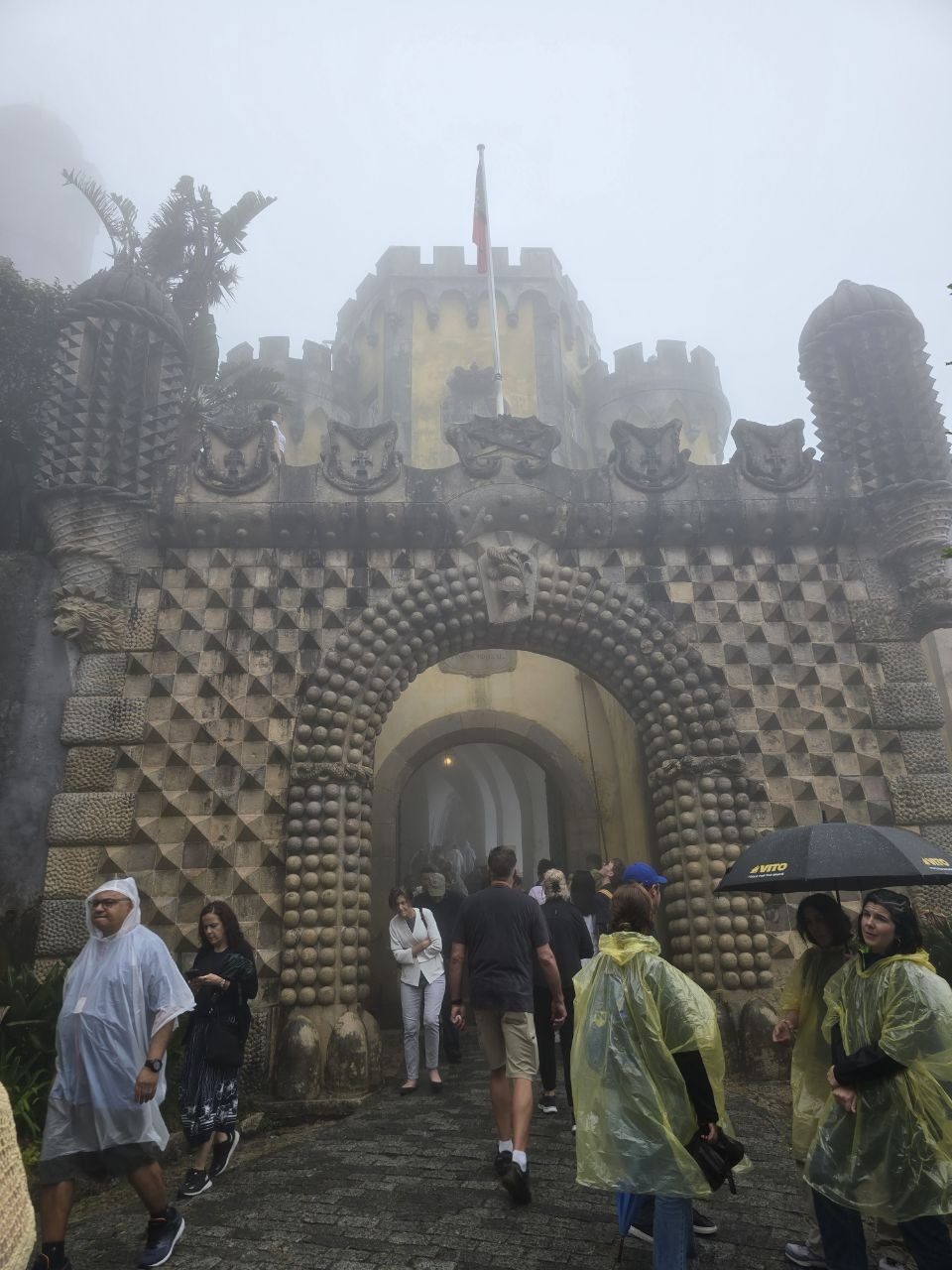 Decorative stone archway and visitors at foggy Pena Palace