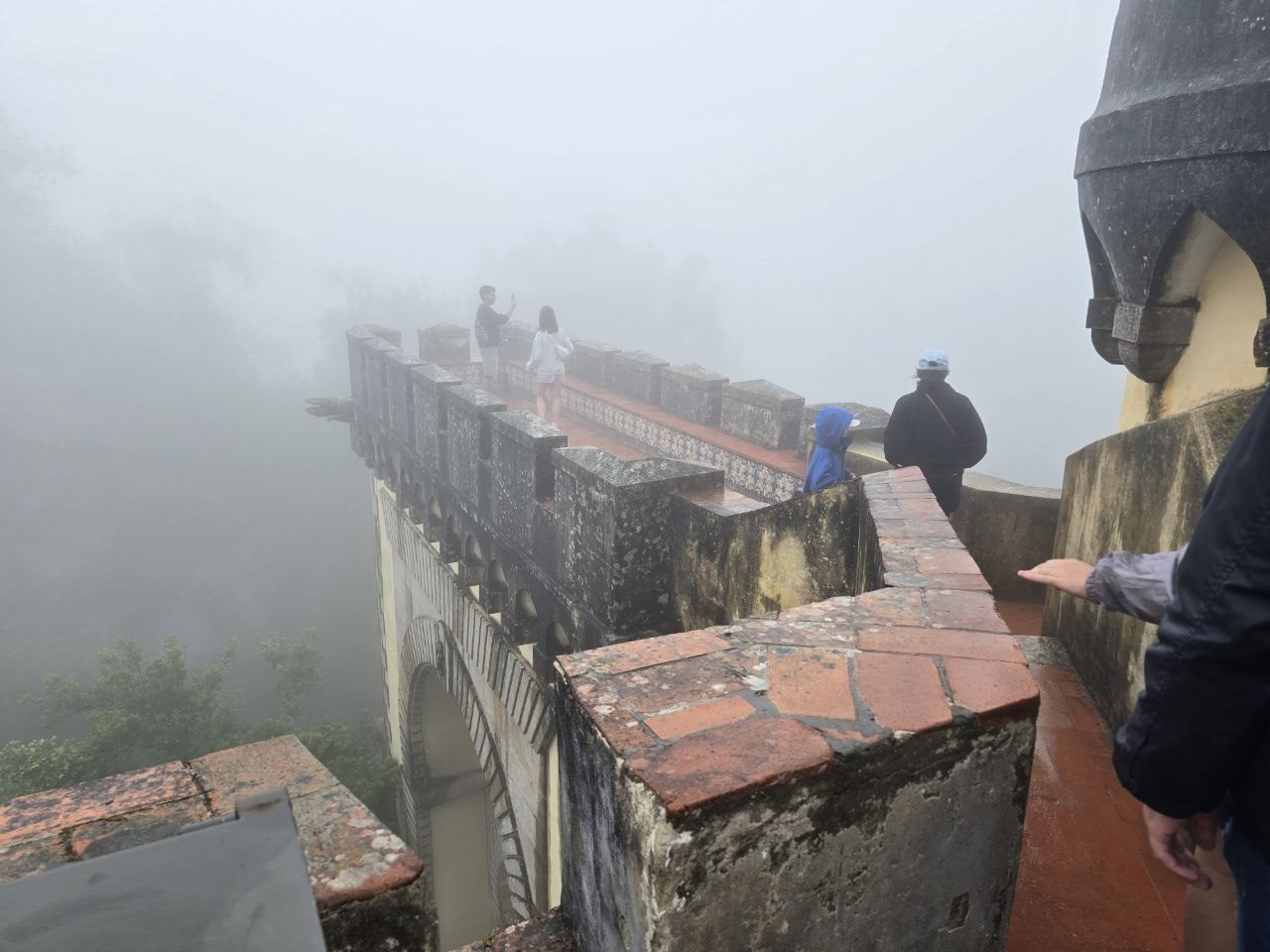 Fog-covered Pena Palace ramparts and visitors with umbrellas