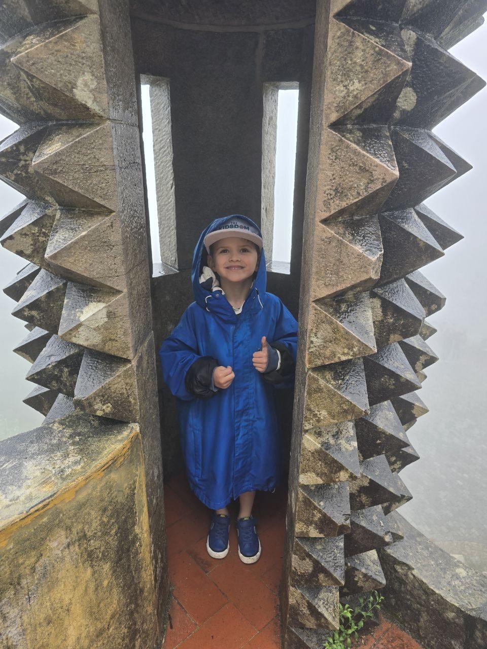 Noah in a blue rain suit standing in a small palace doorway