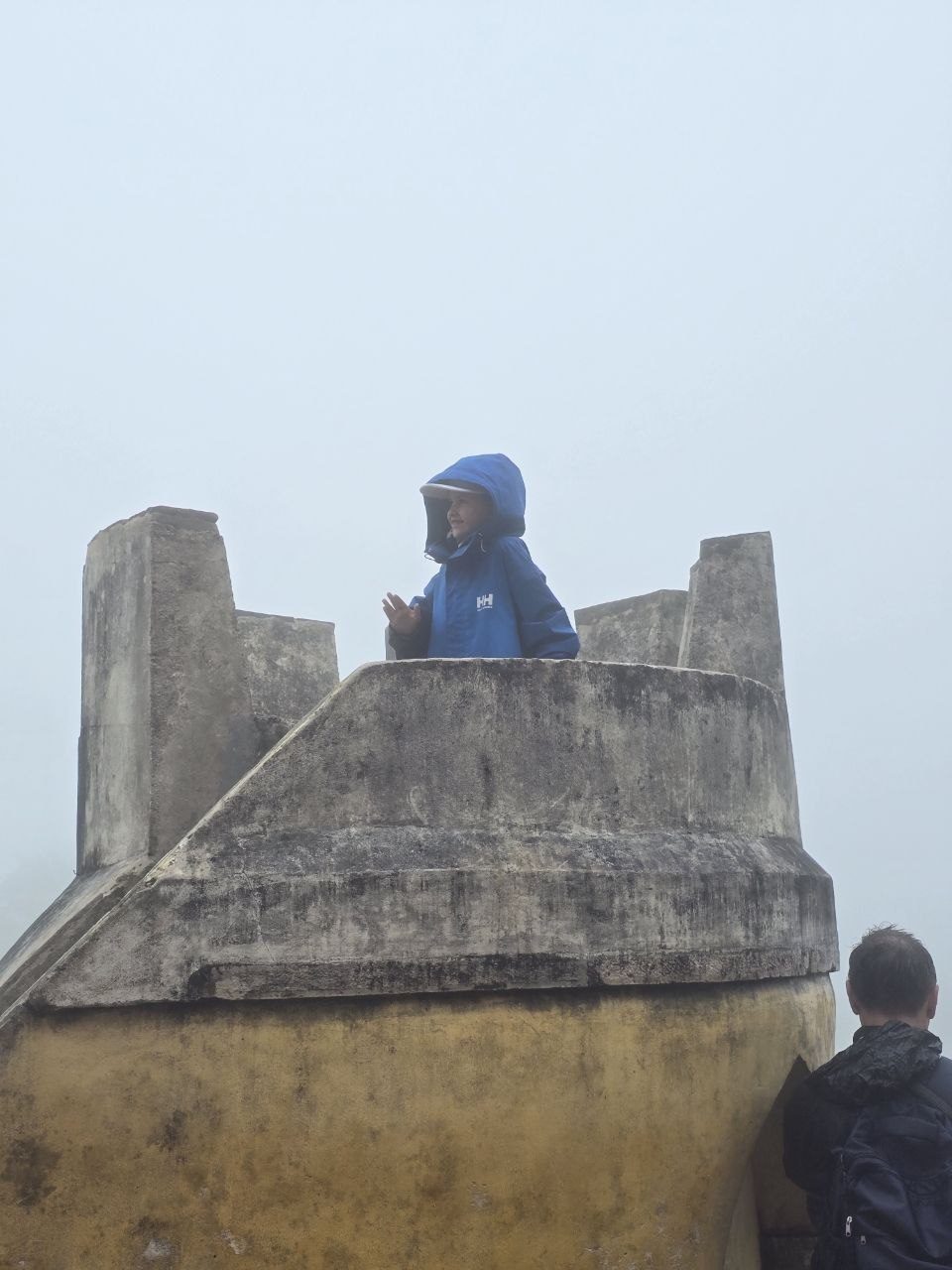 Noah in blue rain gear standing on a stone rampart in fog