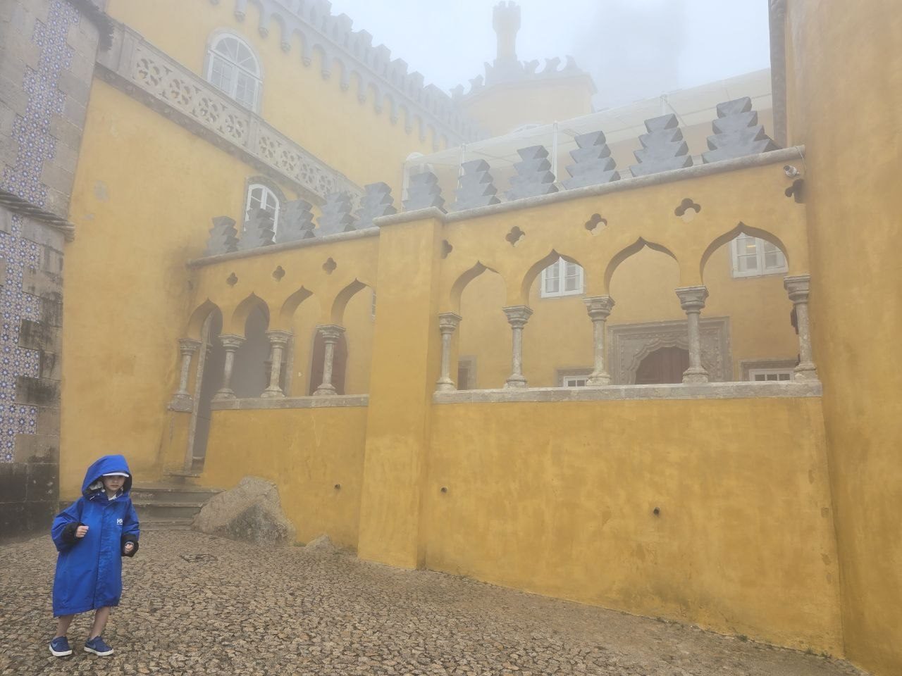 Noah in rain gear standing in a yellow palace courtyard