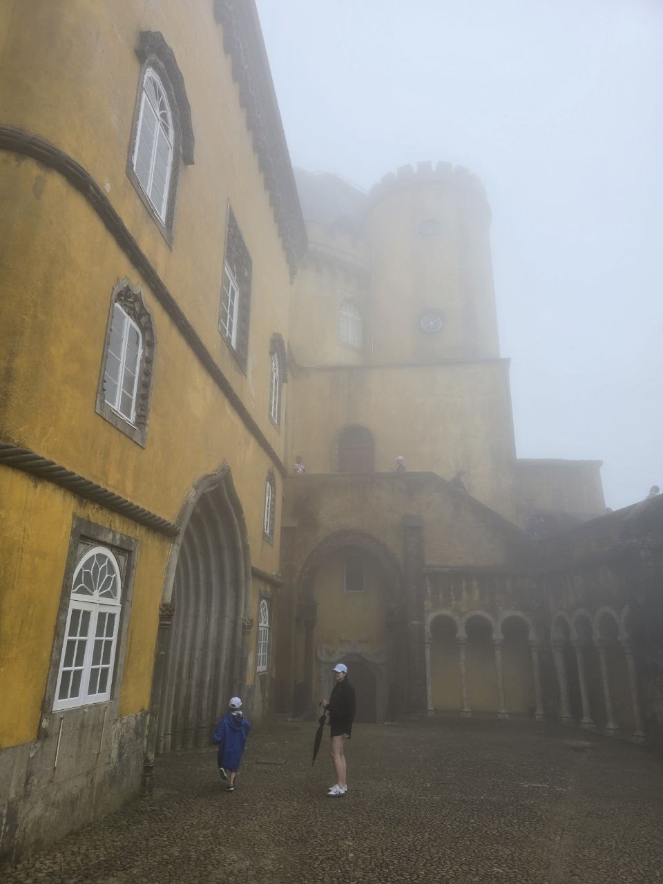 Visitors walking through yellow Pena Palace walls in fog