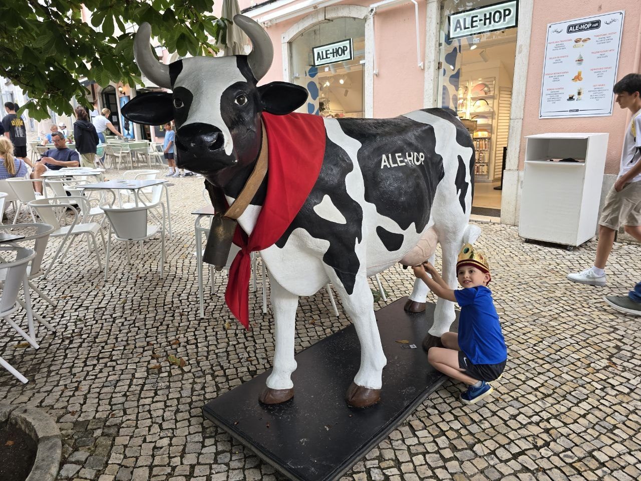 Noah crouching beside a painted cow statue on a cobblestone street
