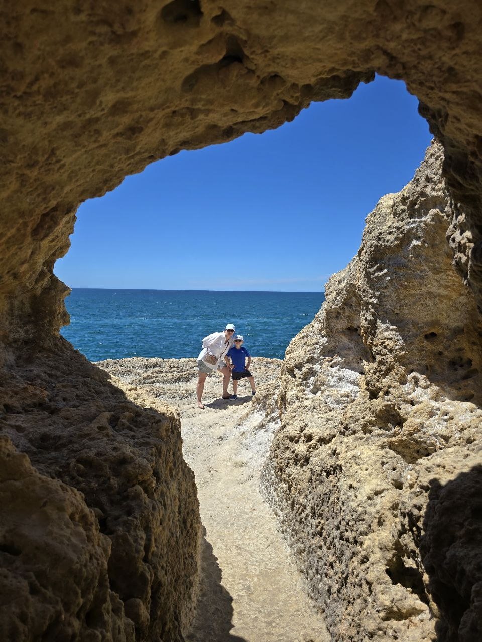 Catherine and Noah framed by a cave opening with ocean behind them