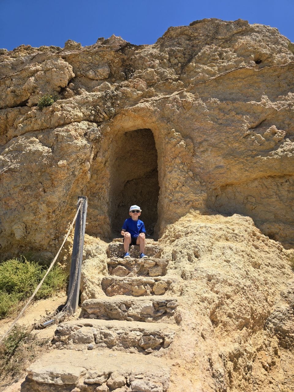 Noah sitting on stone stairs at a small cave entrance