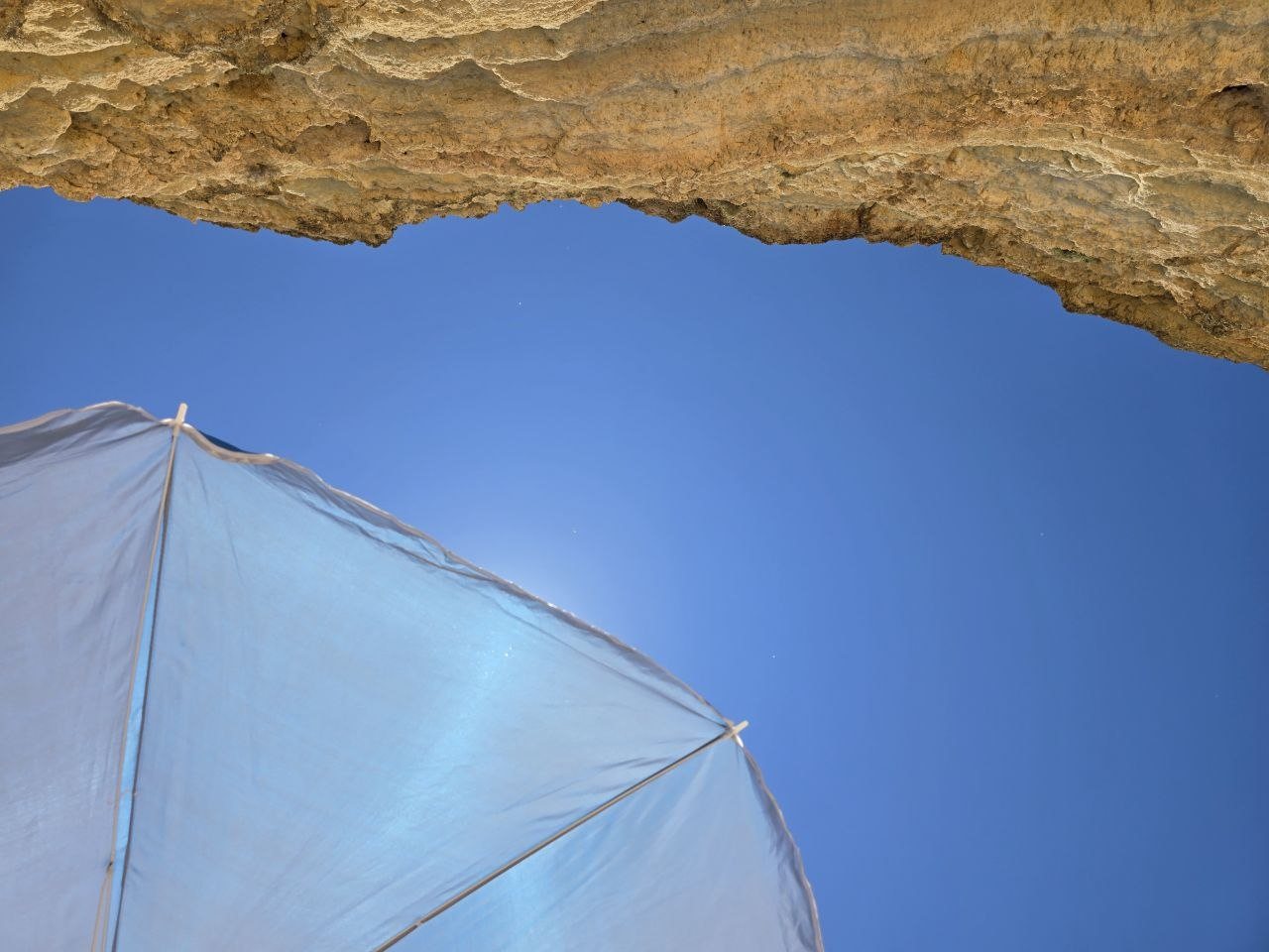 Beach umbrella and golden limestone cliff against a deep blue sky