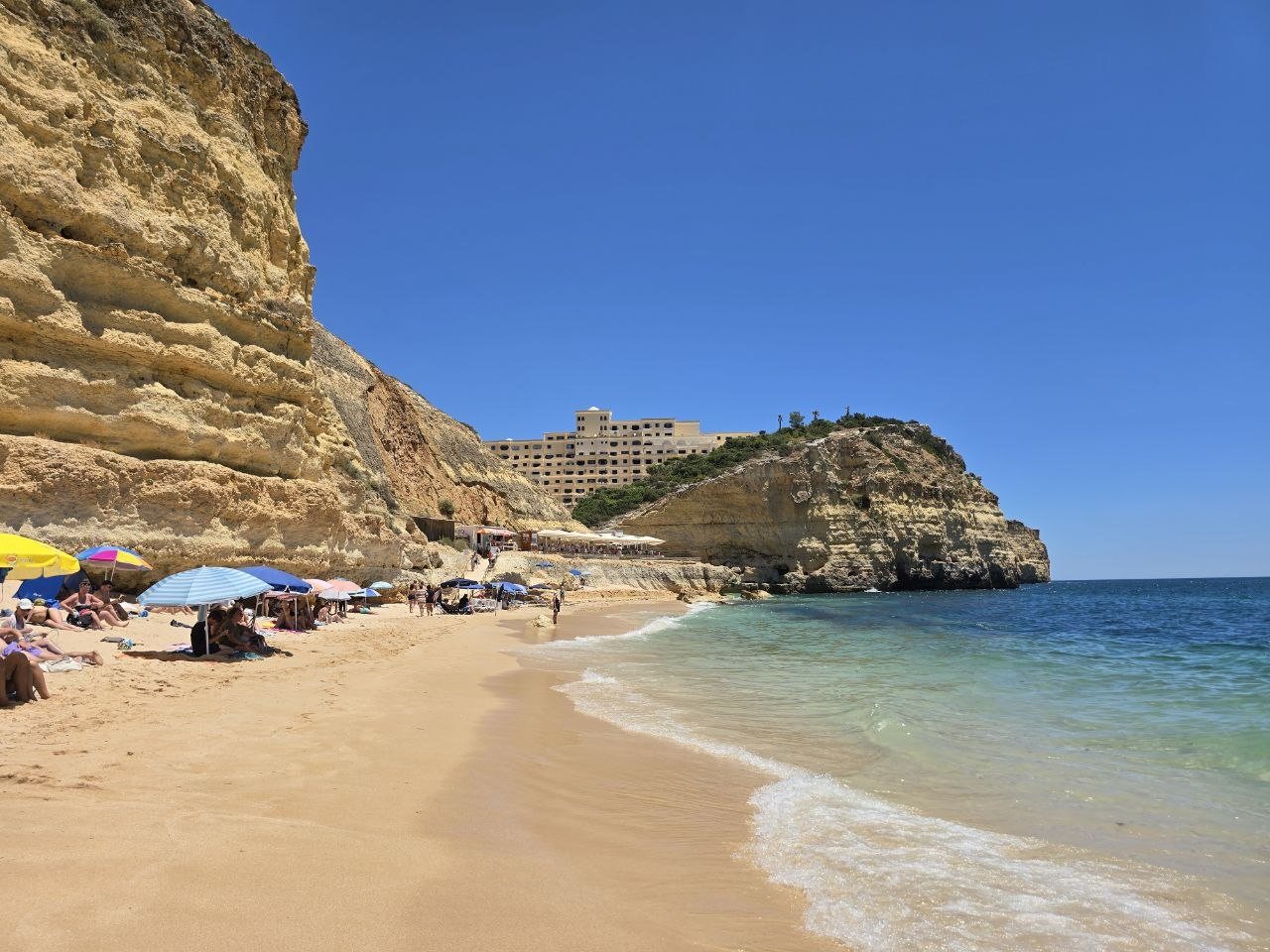 Wide view of Vale de Centeanes Beach with turquoise water, golden cliffs, and beach umbrellas