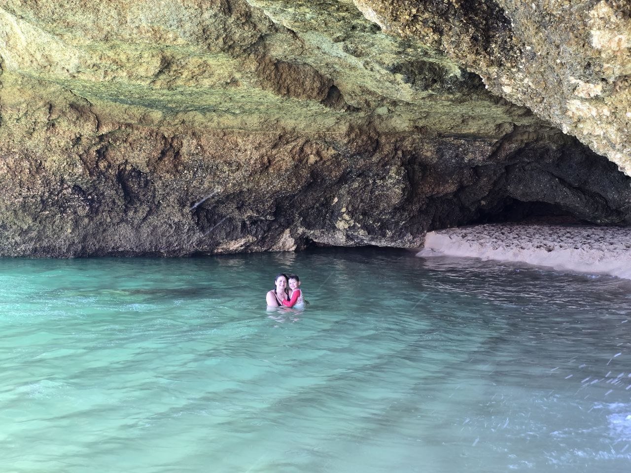 Catherine and Noah floating in turquoise water under a rocky sea cave