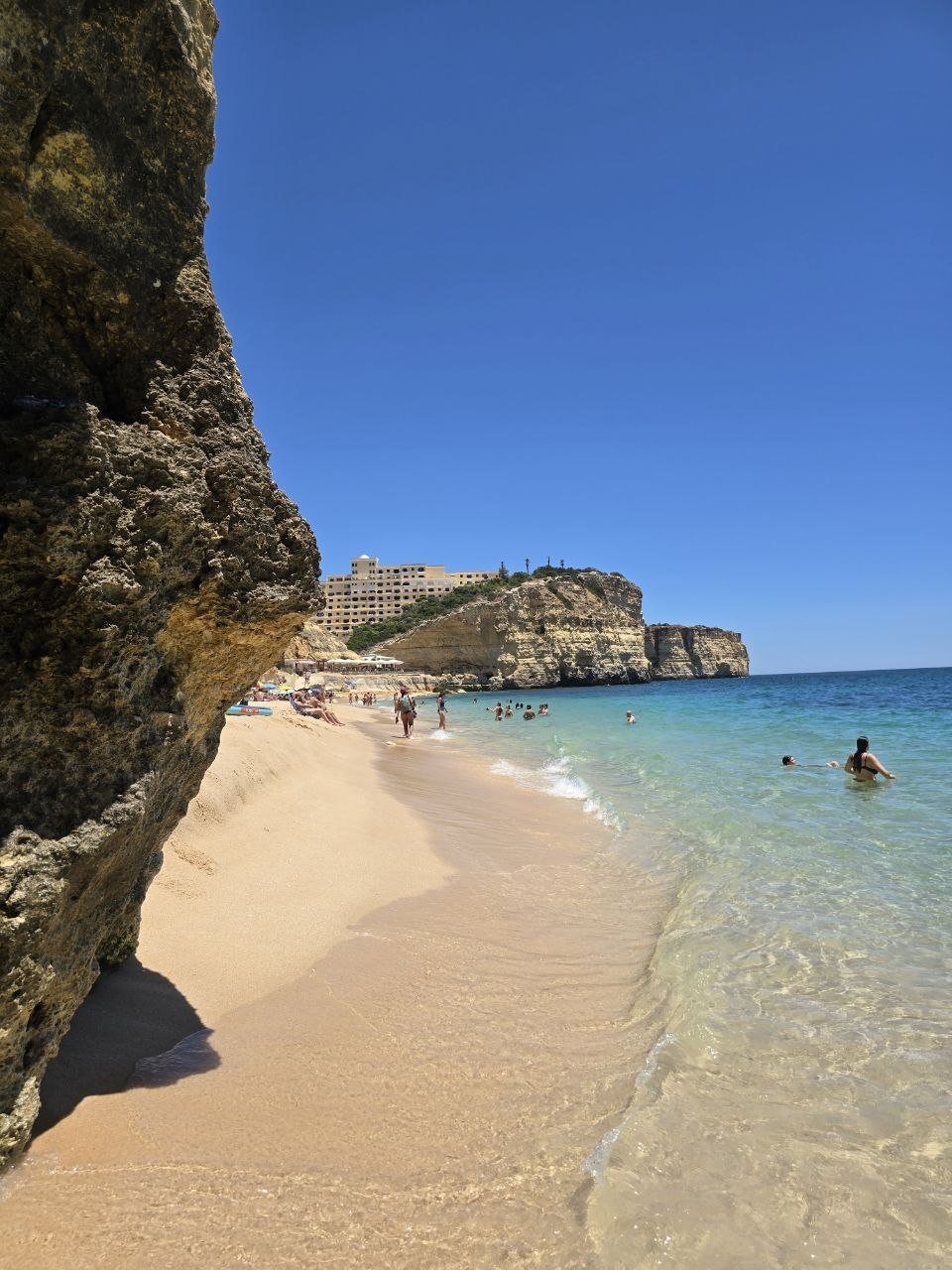 Vale de Centeanes shoreline viewed from beside a dark rock wall with clear water and golden cliffs