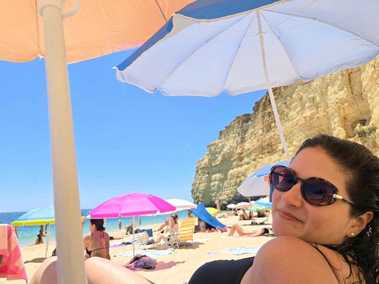 Catherine smiling under a beach umbrella at Vale de Centeanes Beach
