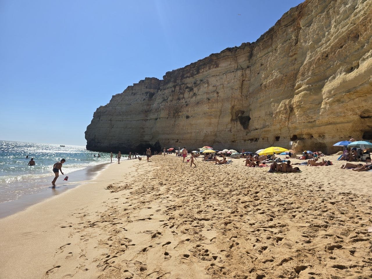 Sunny sandy beach under tall golden cliffs at Vale de Centeanes