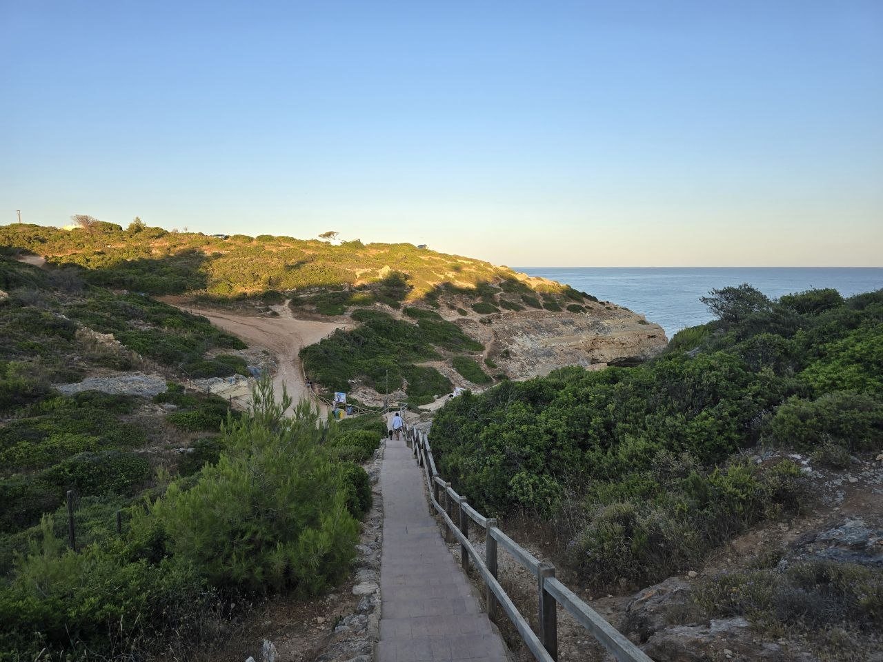 Evening path and stairs down toward Praia do Carvalho with ocean and green cliffs beyond