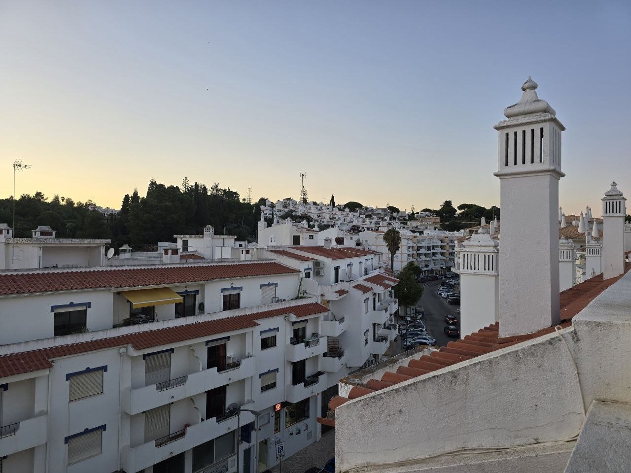 Rooftop terrace view over Carvoeiro apartments, chimneys, and pale sunset sky