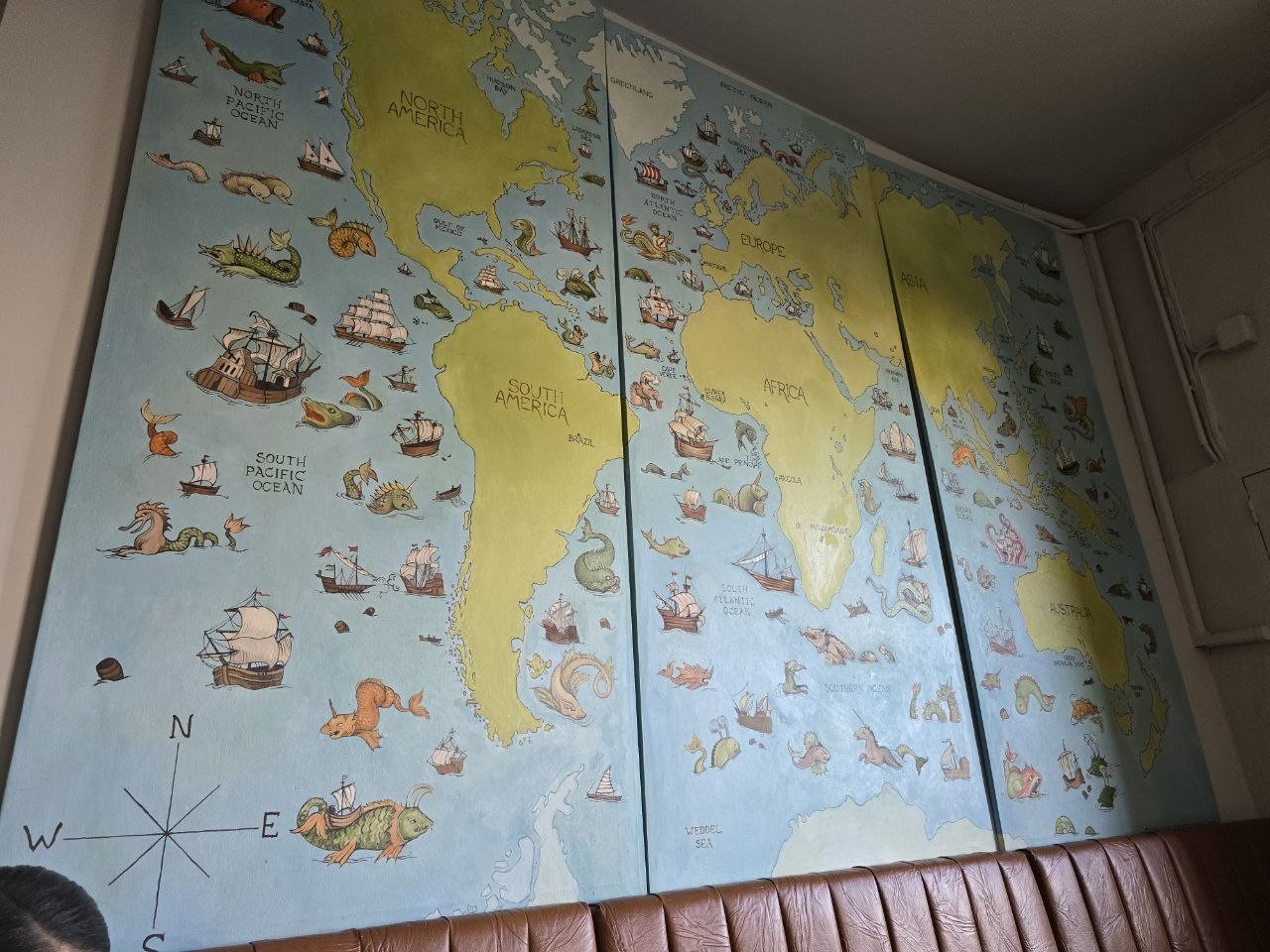 Illustrated world map mural with ships and sea creatures at Restaurante Geographia