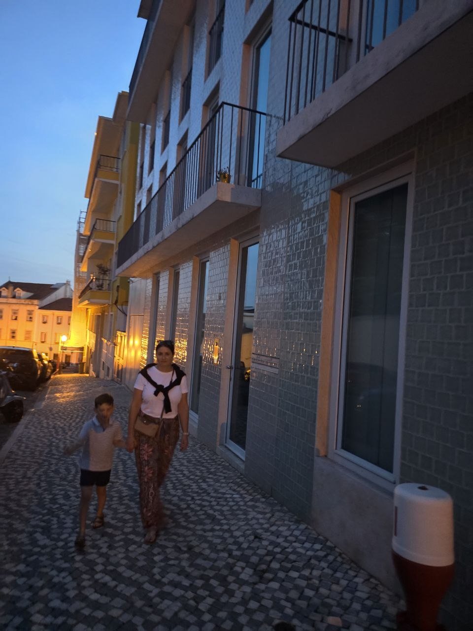 Catherine and Noah walking hand in hand on a Lisbon sidewalk at dusk
